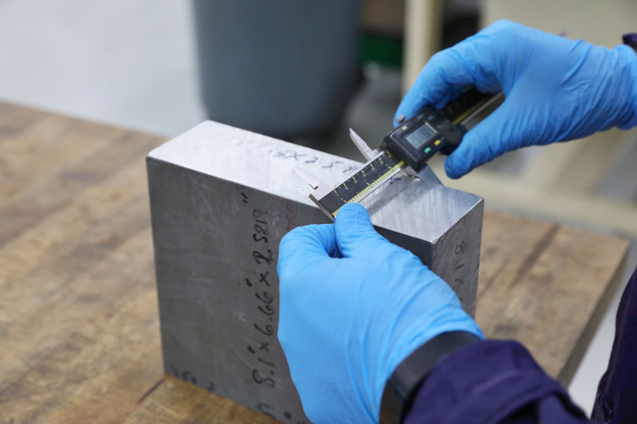 Technician measuring a metal reference block with a digital caliper